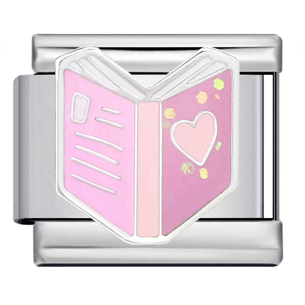 A silver-toned rectangular metal charm link featuring an open pink book design with a heart on the right page and small yellow confetti accents