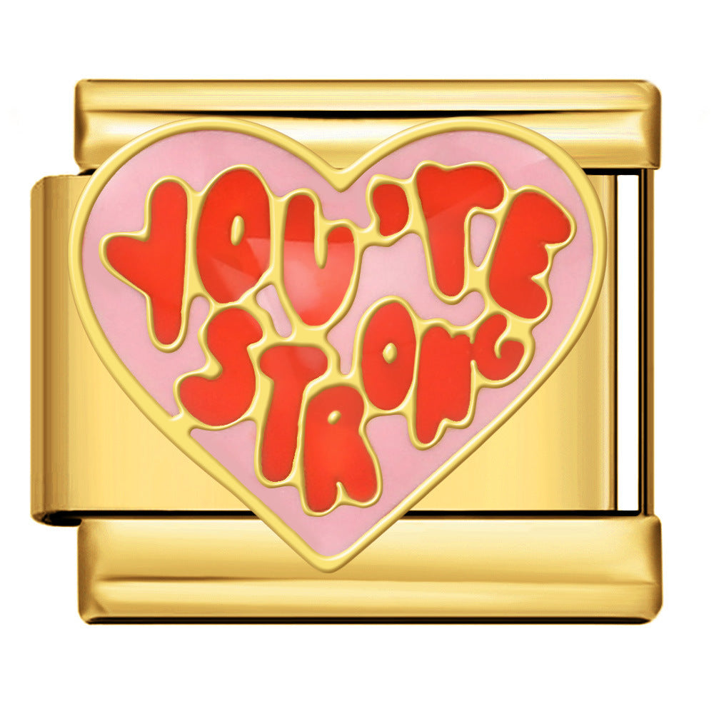 Gold toned charm with a pink heart and red letters saying 'you're strong'